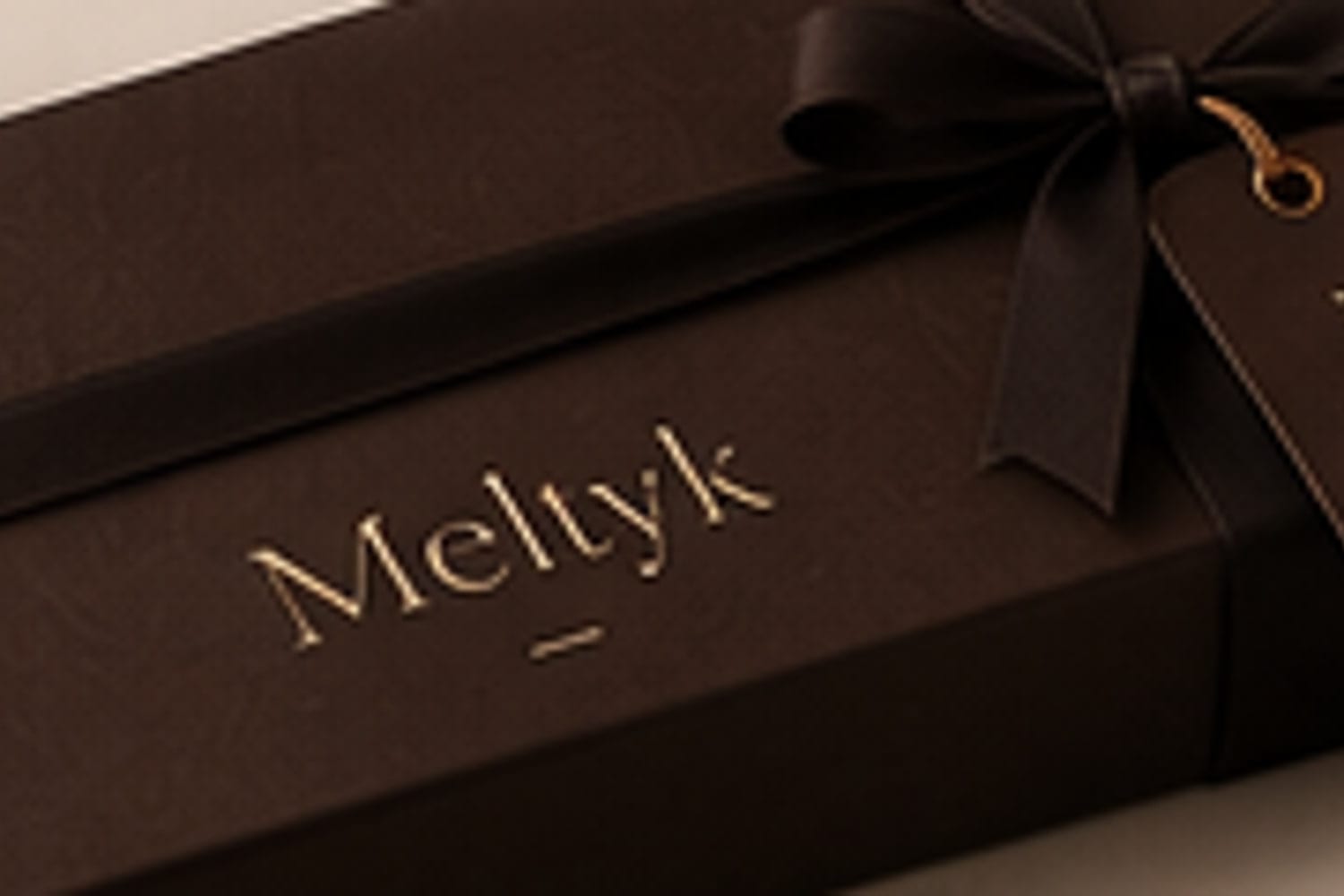 A Meltyk box tied with satin ribbon and a foil-blocked hang tag
